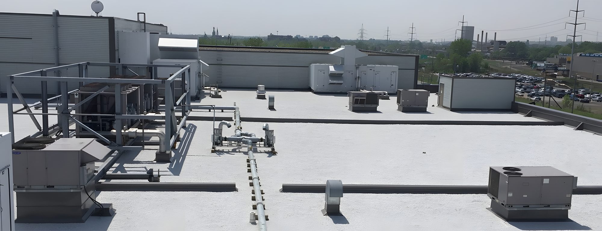 Le toit blanc d'un bâtiment industriel avec ses unités mécaniques et ses conduits, le parc industriel et l'autoroute derrière