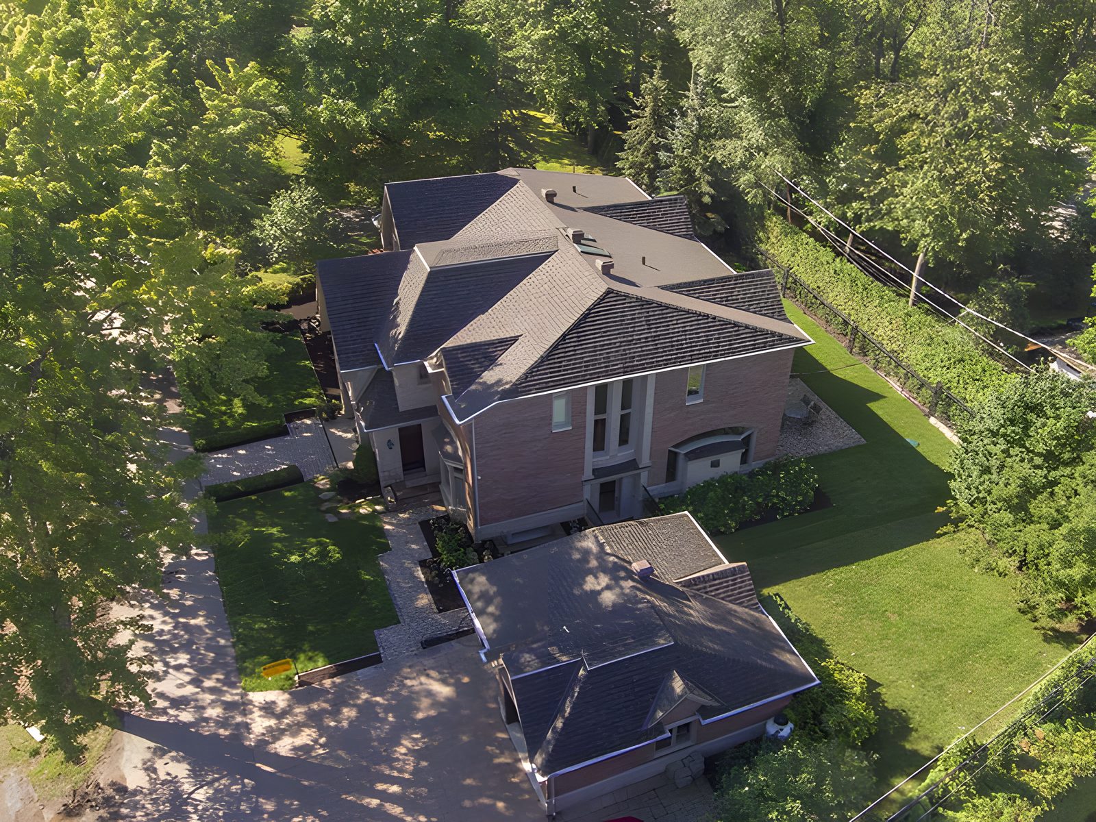 Vue drone d'une grande maison de brique au toit de bardeau gris, entourée d'arbres